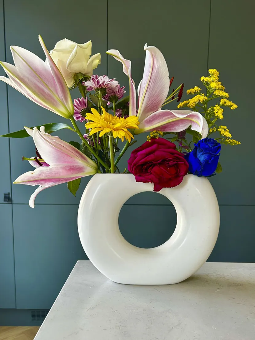 En blomsteroppsats med ulike farger og former i en hvit vase formet som en sirkel.