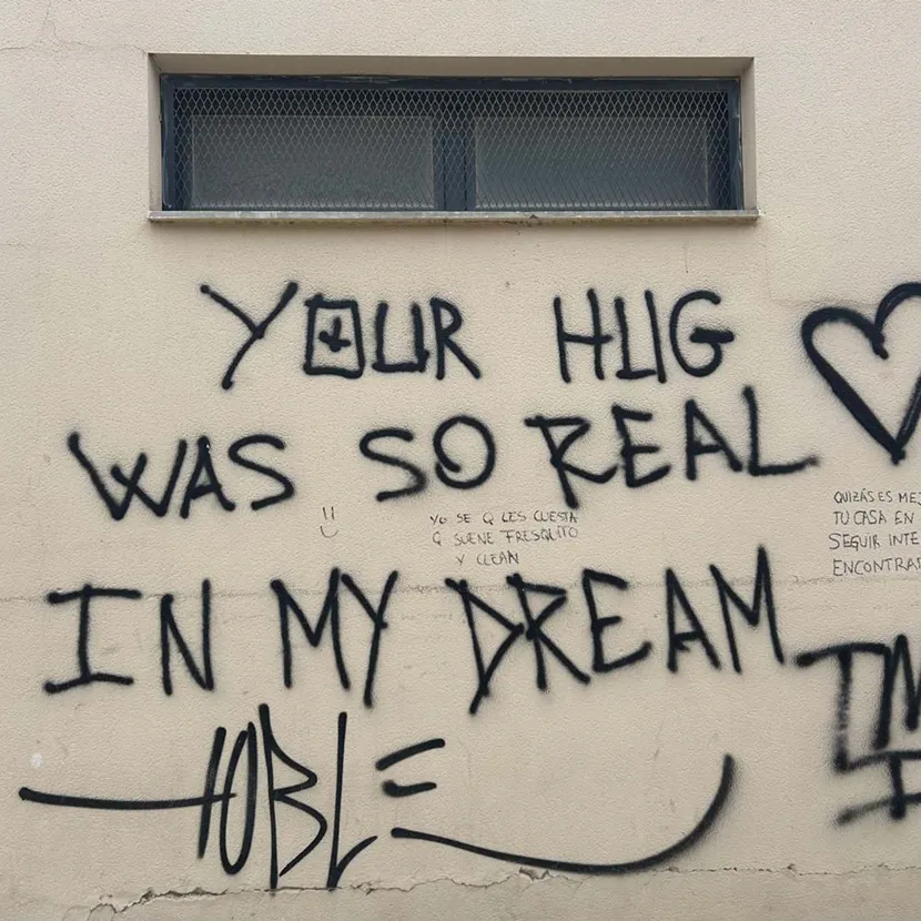 Teksten your hug was so real in my dream, tagget i enkle svarte bokstaver på en lys beige vegg.