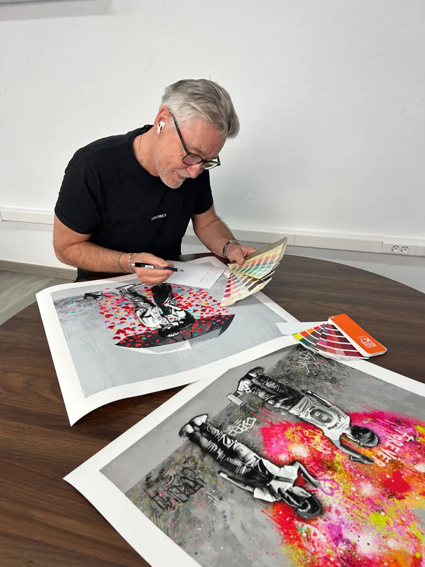 Kunstneren ved et bord, med flere trykk og fargevifter.